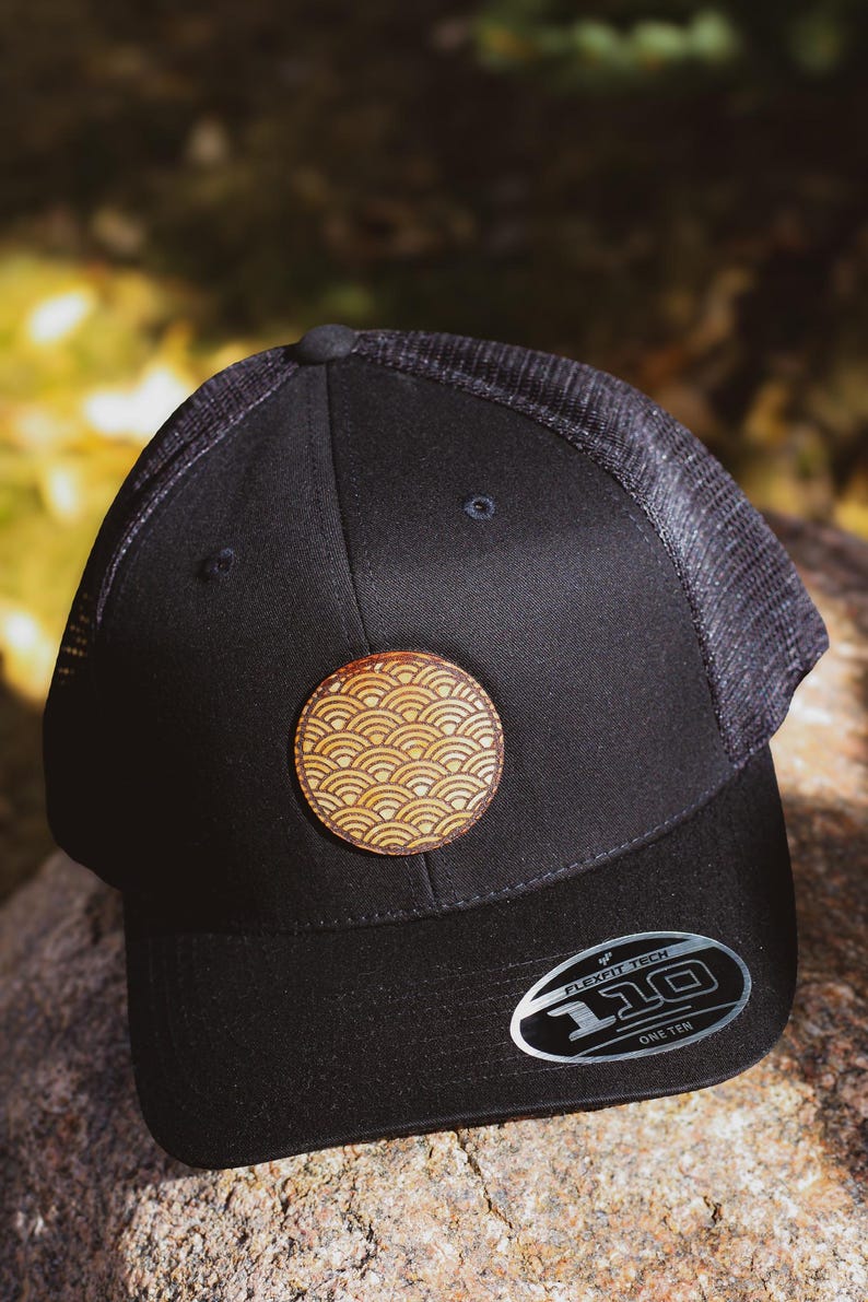 May include: Black mesh and twill baseball cap with a brown leather patch featuring a wave pattern. The cap has a black Flexfit Tech label with the text "110 One Ten".