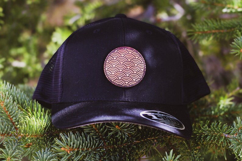 May include: A black mesh trucker hat with a brown leather patch featuring a red and white wave pattern.