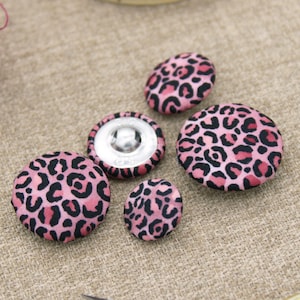 May include: Five pink and black leopard print fabric buttons. The buttons are different sizes and have a variety of patterns.