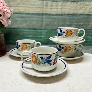 Puede incluir: Juego de cuatro tazas de té y platillos blancos con un diseño de pájaro azul y flores. Las tazas y los platillos tienen un borde azul.