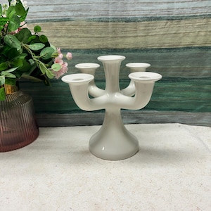 Puede incluir: Un candelabro de cerámica blanca con cinco portavelas. El candelabro tiene un diseño único y moderno con una base ancha y cinco brazos que se extienden desde el centro.