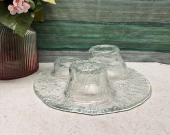 May include: A set of three clear glass candle holders with a textured surface. The candle holders are arranged in a circle on a white surface.