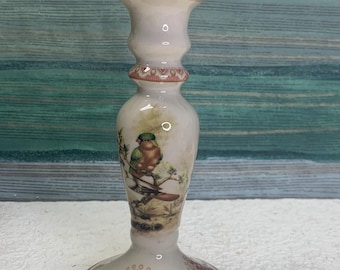 May include: White ceramic candle holder with a pink and white floral design and a bird illustration. The holder has a wide base and a narrow top.