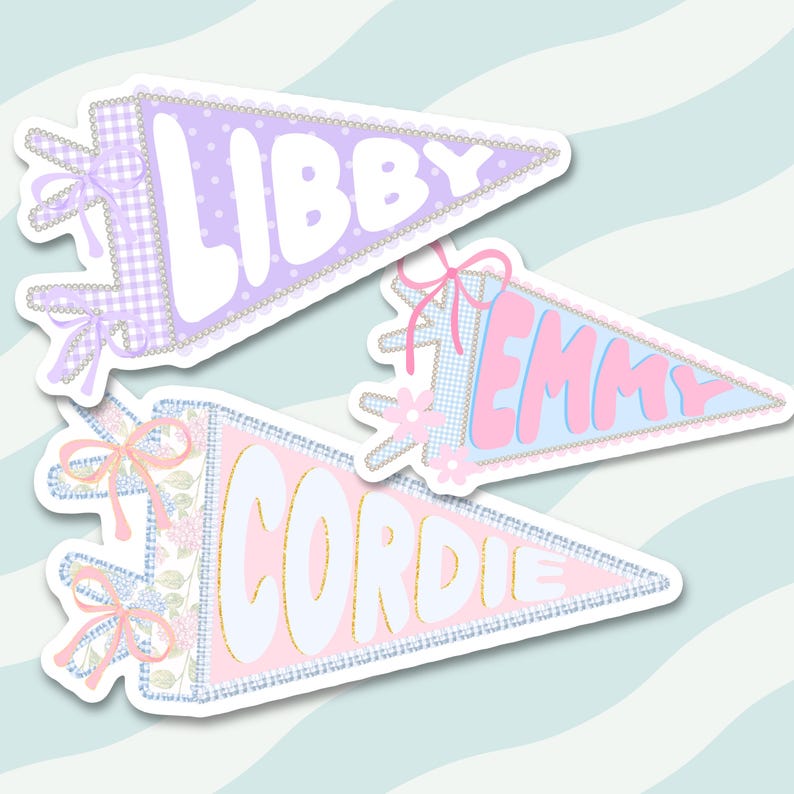 Pode incluir: Tr&ecirc;s autocolantes em forma de bandeirola triangular com bordas decorativas e la&ccedil;os. A bandeirola superior &eacute; lavanda com bolinhas brancas e o nome LIBBY. A do meio &eacute; azul claro com o nome EMMY. A inferior &eacute; rosa com o nome CORDIE.