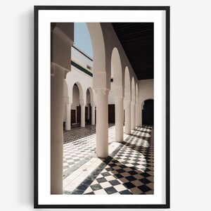 May include: A framed wall art print featuring a series of white architectural arches and columns. The floor is covered in a black and white checkered tile pattern, creating long, dramatic shadows that stretch across the ground in the sunlight.
