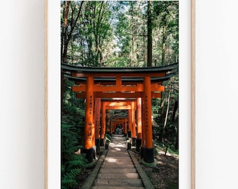 May include: A vertical framed wall art print featuring a path lined with vibrant orange torii gates leading into a dense green forest. The structure consists of multiple wooden gates with black accents, creating a tunnel effect along a stone walkway.