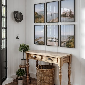 May include: A wooden console table with two drawers and turned legs, a woven basket, and two potted plants. Six framed photographs of seascapes hang on the wall behind the table.