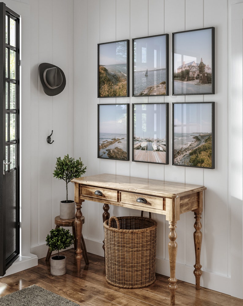 May include: A wooden console table with two drawers and turned legs, a woven basket, and two potted plants. Six framed photographs of seascapes hang on the wall behind the table.