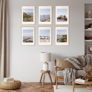 May include: Six framed photographs of coastal scenes, including a harbor with boats, a beach with rocks, and a building with a white facade. The photos are arranged in a grid pattern on a white wall.
