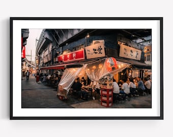 May include: A street-level view of a Japanese izakaya restaurant at dusk, featuring outdoor seating protected by clear plastic curtains, red signage with Japanese characters, a bright orange paper lantern, and stacks of red plastic crates.