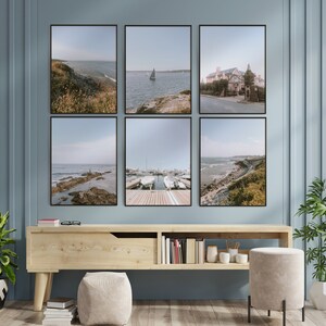 May include: A set of six framed photographs of a coastal scene with a blue sky, water, and green foliage. The photos are arranged in a grid pattern on a light blue wall above a wooden shelf.