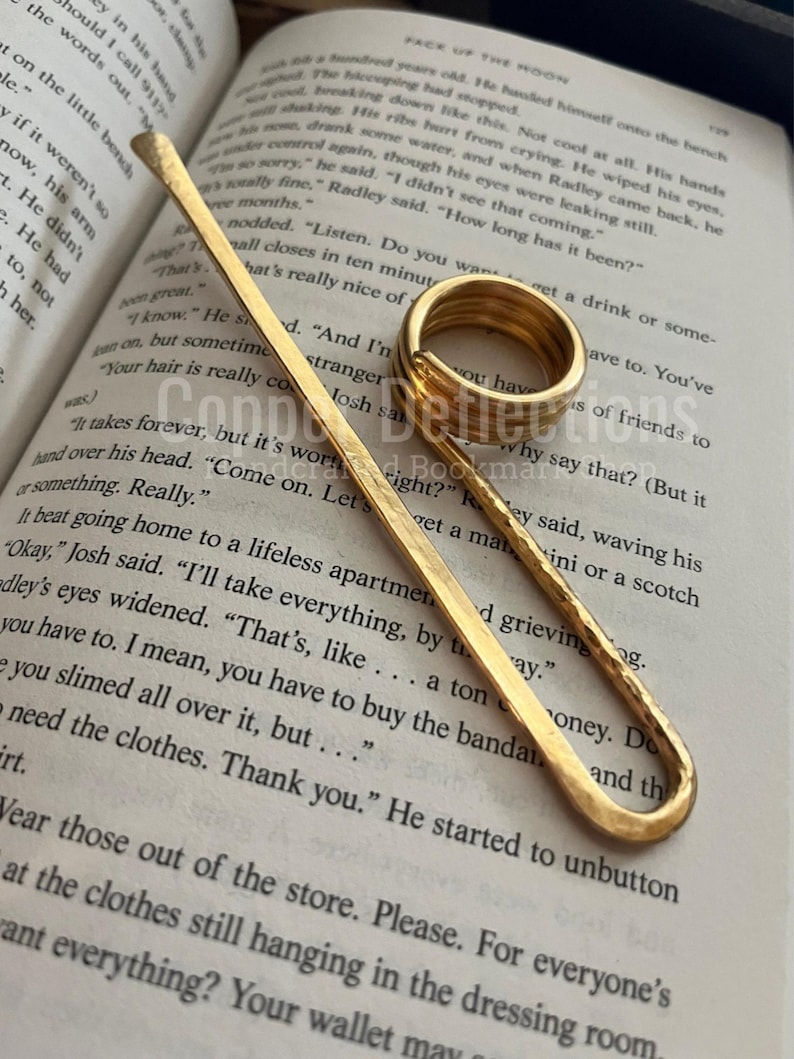 Puede incluir: Dos marcap&aacute;ginas de metal dorado. Uno es un marcap&aacute;ginas largo, delgado y recto. El otro es un marcap&aacute;ginas m&aacute;s grueso, redondeado y con un bucle abierto. Ambos marcap&aacute;ginas est&aacute;n sobre un libro con texto.