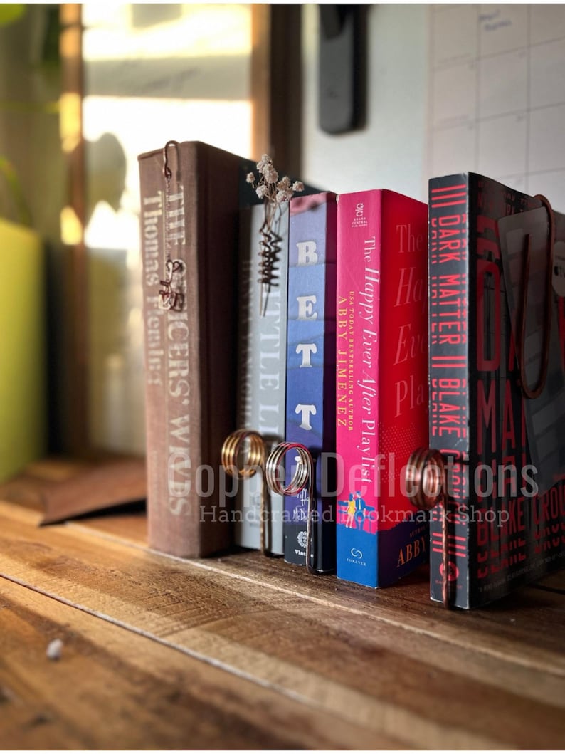 May include: A set of bookends made of copper wire, holding up a collection of books with various titles. The bookends are shaped like a pair of rings, and the books are all different colors and sizes.
