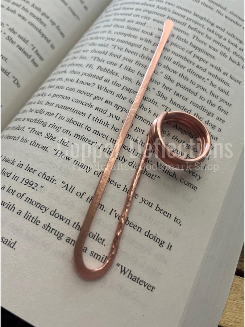 Puede incluir: Dos anillos de cobre con las palabras "Angela" y "He's that good guy b" grabadas en ellos. Los anillos est&aacute;n sobre un libro con texto sobre un anillo de boda.