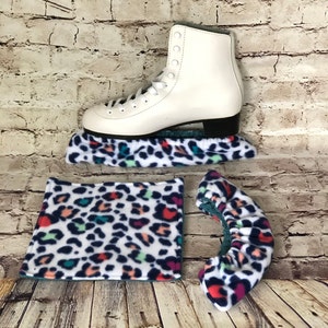 Op de afbeelding: Witte kunstschaatsen met een luipaardprint fleece schaatsbeschermer, teenbeschermer en beschermer voor de schaats.