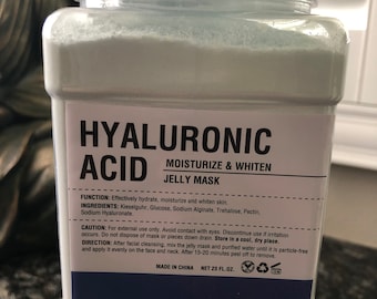May include: A white plastic jar with a blue label that reads "HYALURONIC ACID MOISTURIZE & WHITEN JELLY MASK". The label also includes the ingredients, directions, and cautions for use. The jar contains a white powder and is labeled "NET 23 FL.OZ.".