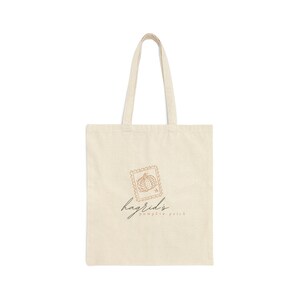 May include: Cream-colored tote bag with a pumpkin stamp design and the text "hagrid's pumpkin patch" in a script font. The bag has two handles and is made of a sturdy fabric, perfect for carrying groceries or books.