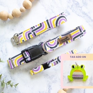 May include: Three dog collars and a tag. The collars have a repeating pattern of yellow, purple, and black curved lines on a white background. The tag is a green frog with a non-binary flag design.