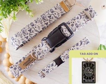 May include: A set of three dog collars and a matching keychain. The collars and keychain feature a cream-colored fabric with a repeating black pattern of moons, stars, and botanical elements. The collars have black plastic buckles and metal hardware.