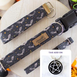 May include: A black fabric collar and matching keychain featuring a pattern of grey bats and yellow stars. The collar includes a black plastic buckle, a metal D-ring, and a tan label reading citrine sunrise. An inset shows a round black tag with a white pentagram.