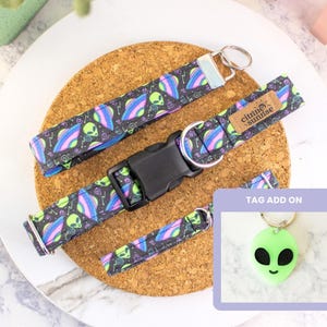 May include: A dog collar, leash, and keychain set with an alien theme. The black fabric features neon green, purple, and blue alien heads and flying saucers. The set includes a black buckle and a green alien head tag.