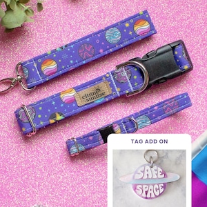 May include: Purple dog collar and leash set with a planet pattern. The collar has a black buckle and a metal D-ring. The leash has a metal clasp. A matching tag with the words "SAFE SPACE" is also included.