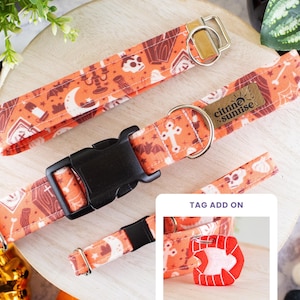 May include: An orange pet collar featuring a repeating pattern of skulls, coffins, bats, moons, and candles. The collar has a black plastic buckle, a silver metal D-ring, and a brown leather tag labelled Citrine Sunrise. Includes a red vampire teeth tag.