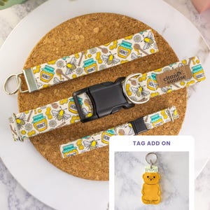May include: A fabric wristlet, a dog collar with a black plastic buckle and a brown brand tag reading Citrine Sunrise, and a matching leash, all featuring a pattern of bees, honey jars, and flowers. Includes a bear-shaped tag add-on.
