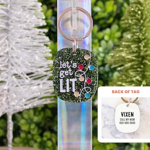 May include: A dark green glittery pet tag keychain with a silver metal ring. The front features the white text "let's get LIT" with a string of colorful light bulbs. The back of the tag is white with the black text "VIXEN", "CALL MY MOM", and "000-000-0000".
