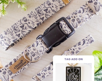 May include: A pet collar featuring a dark gray pattern of moons, stars, eyes, and plants on a light fabric. It includes a black plastic buckle, a metal D-ring, and a tan leather tag labeled citrine sunrise. An inset shows a rectangular tag labeled THE MOON.