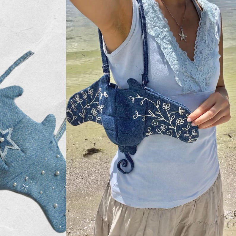 May include: A blue denim handbag shaped like a manta ray with white embroidered floral details. The bag is worn by a person with a light blue tank top and a white lace trim.
