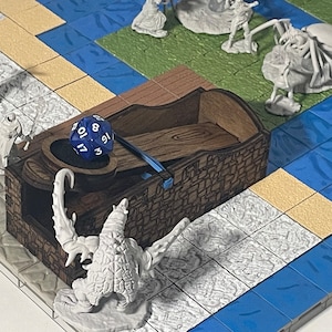 Puede incluir: Una torre de dados de madera con un dado azul y blanco en su interior. La torre está decorada con un diseño de pared de piedra y una escultura de escorpión. La torre de dados está sobre un tablero de juego con azulejos azules y blancos.