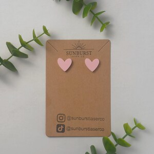 May include: A pair of pink heart-shaped earrings on a brown card with the text "SUNBURST LASER CO" and social media handles for @sunburstlaserco.