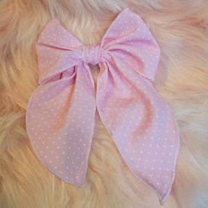 May include: A pink bow with white polka dots. The bow is made of fabric and has a satin finish.