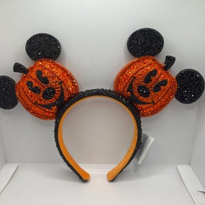 May include: Black and orange Mickey Mouse ears headband with pumpkin-shaped ears covered in rhinestones.