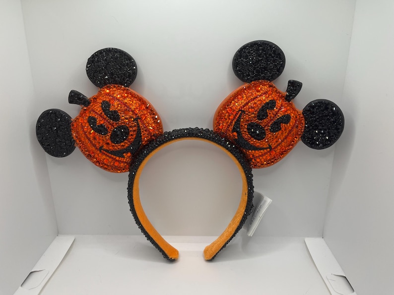 May include: Black and orange Mickey Mouse ears headband with pumpkin-shaped ears covered in rhinestones.