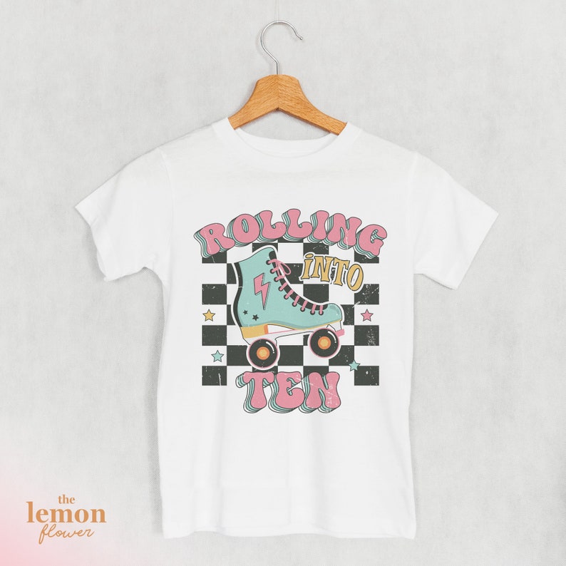 May include: White t-shirt with a graphic design of a roller skate with the text "Rolling into Ten" in pink and blue retro font.