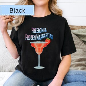 May include: Black t-shirt with the text "Freedom & Frozen Margaritas" in blue and white. A red margarita glass with a strawberry garnish is featured below the text. The shirt has a relaxed fit.
