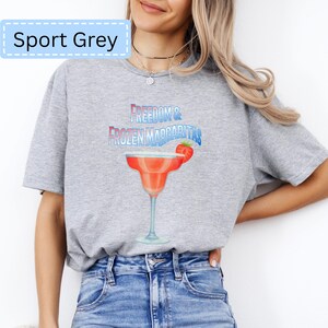 May include: Sport Grey t-shirt with the text "Freedom & Frozen Margaritas" above a margarita glass illustration. The margarita is red with a strawberry garnish. The shirt is a light grey color.