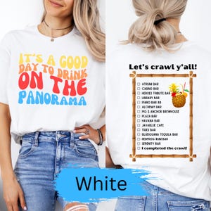 May include: White t-shirt with the text "It's a good day to drink on the panorama" in rainbow colors. A second white t-shirt with a list of bars and the text "Let's crawl y'all!" and "I completed the crawl!"