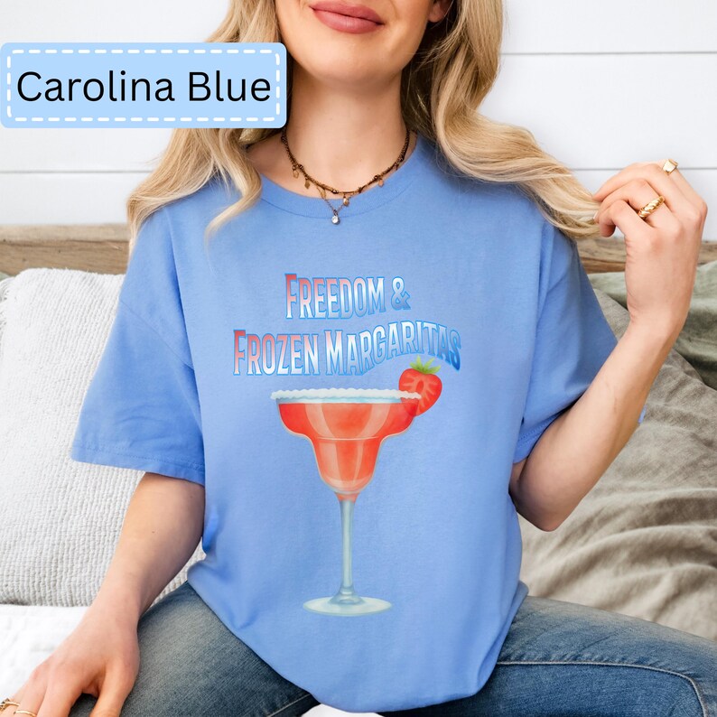 May include: Carolina Blue t-shirt with the text "Freedom & Frozen Margaritas" and a margarita glass graphic. The margarita glass is red with a strawberry garnish. The shirt is a light blue color.