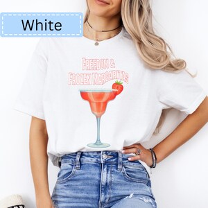 May include: White t-shirt with the text "Freedom & Frozen Margaritas" and a watercolor illustration of a margarita cocktail. The margarita glass is red with a blue rim and a strawberry garnish.