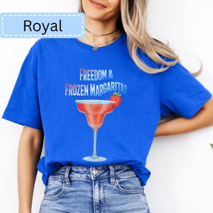 May include: Royal blue t-shirt with the text "Freedom & Frozen Margaritas" and a graphic of a margarita glass with a strawberry garnish. The shirt is a solid color and has short sleeves.