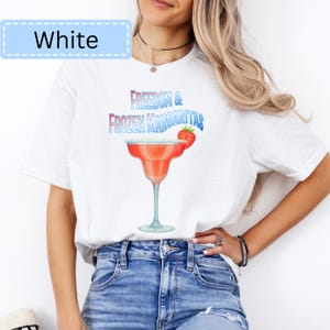 May include: White t-shirt with a graphic of a margarita cocktail and the text "Freedom & Frozen Margaritas". The margarita is red with a strawberry garnish. The word "White" is in a light blue box at the top left.