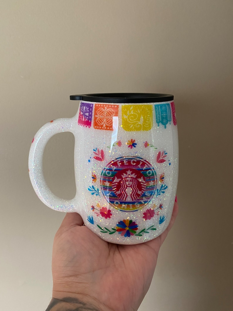 May include: White glitter tumbler with a black lid and a colorful Mexican-inspired design featuring a Starbucks logo with the text "F&Eacute;CITO" and "ORIGINS".
