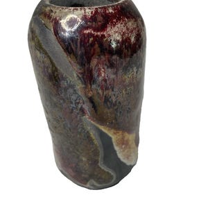 Puede incluir: Un jarrón cilíndrico de cerámica con un esmalte complejo en tonos burdeos profundo, marrón oscuro y gris apagado. La superficie muestra un aspecto texturizado y moteado con una franja diagonal distintiva de color gris mate.