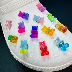 May include: A white shoe with colorful gummy bear charms attached. The charms are in various colors, including pink, blue, green, yellow, orange, and purple.