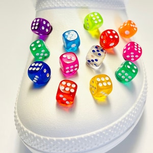 May include: A white shoe with colorful dice charms attached. The dice are translucent and have white dots. The colors of the dice are red, orange, yellow, green, blue, purple, and pink.