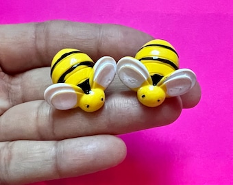 Op de afbeelding: Twee gele en zwarte bij-vormige oorbellen met witte vleugels. De oorbellen zijn gemaakt van plastic en hebben een glanzende afwerking.