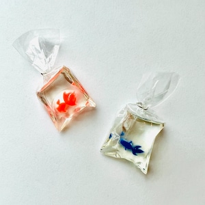 May include: Two clear, fish-shaped resin pendants, each resembling a goldfish in a plastic bag. One pendant features a bright orange fish, the other a blue fish. The bags have a clear, twisted top.